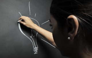 Una bella ragazza disegna una lampadina alla lavagna